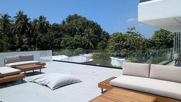 Eine Dachterrasse mit Sitzgelegenheiten im Freien, einer Glasbrüstung und Blick auf eine tropische Landschaft.
