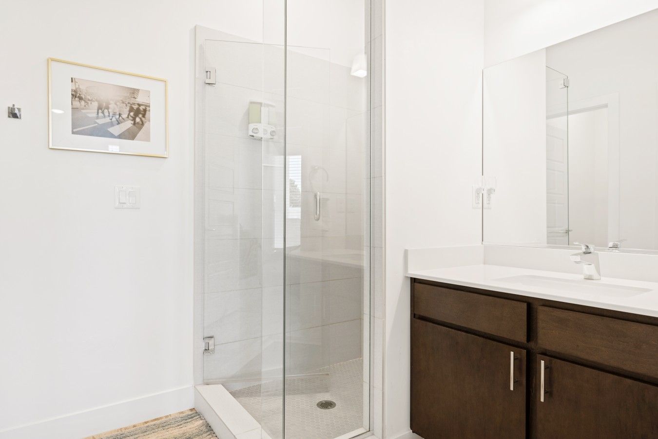 A modern bathroom with a glass shower enclosure, a white sink, and a dark wooden vanity.