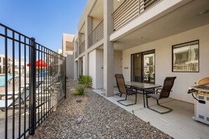 A patio area with a grill, outdoor seating, and a view of a swimming pool.