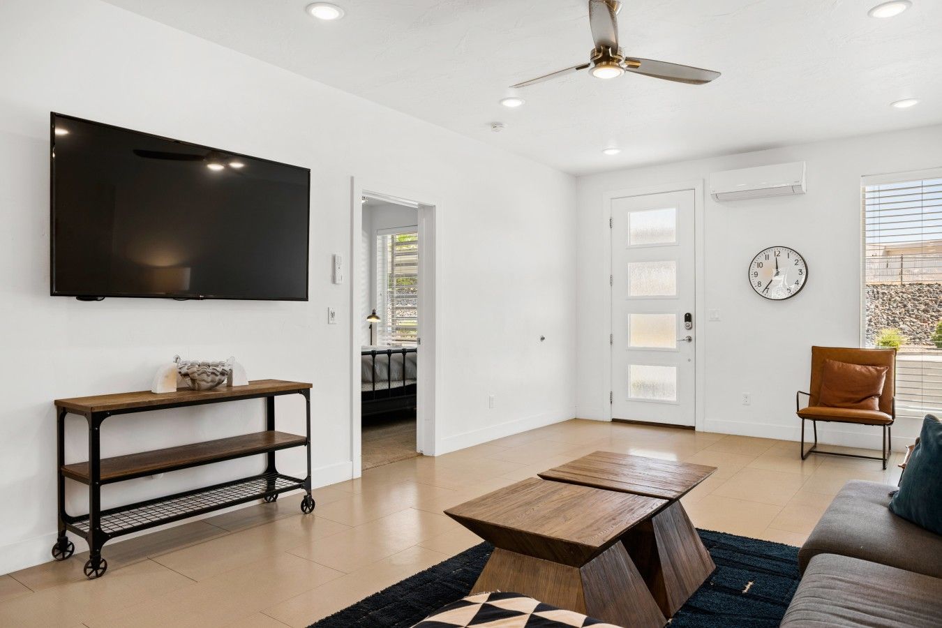 A modern living room with a flat-screen TV, a coffee table, a sofa, a chair, and a door leading to another room.