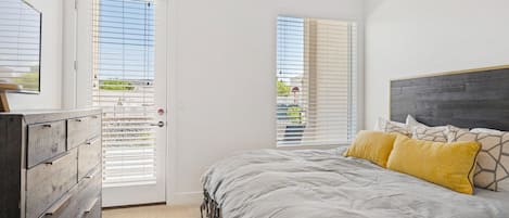 A bedroom with a bed, a dresser, and two windows with blinds.