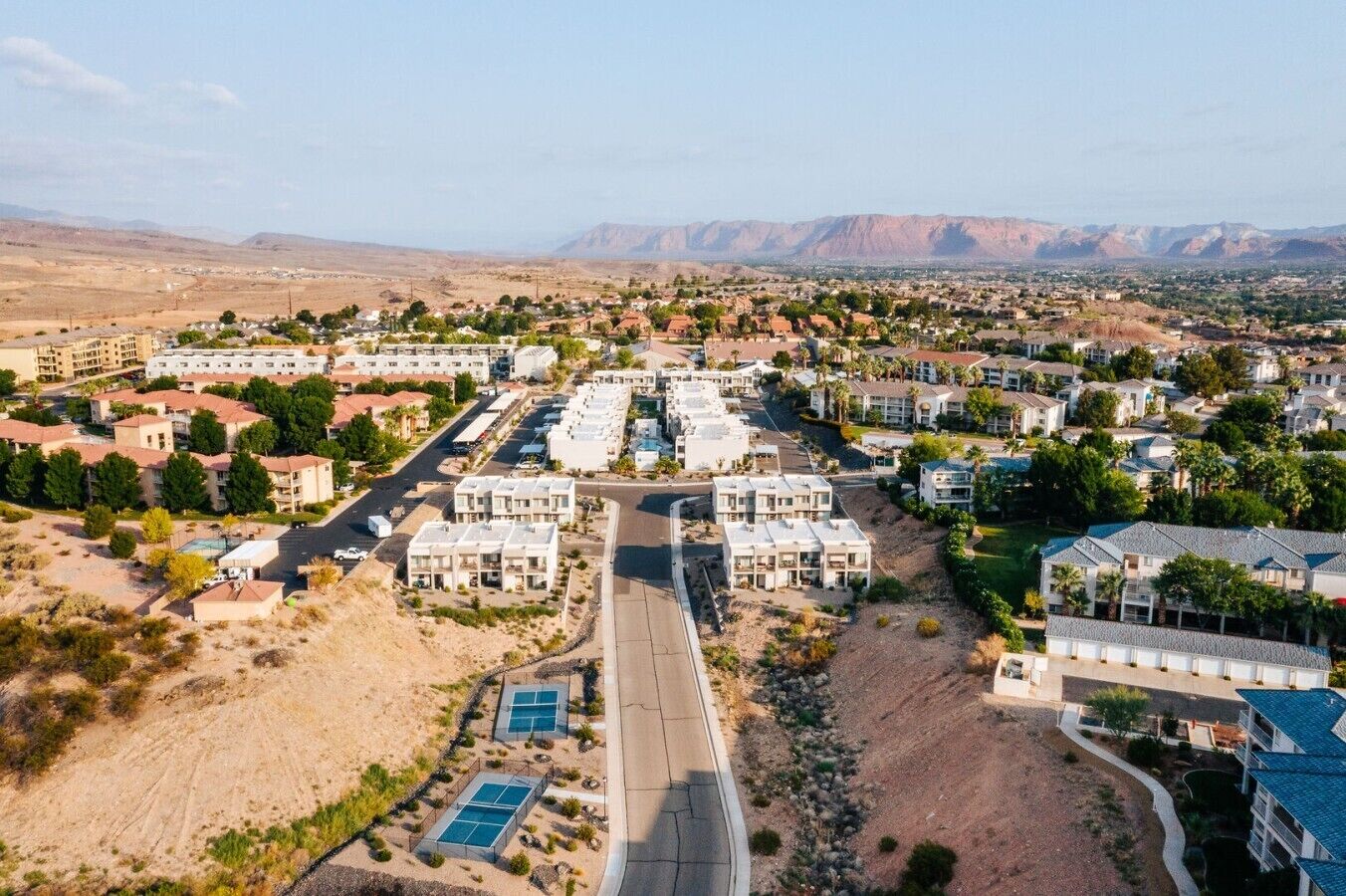 A residential area with modern apartment buildings, a central road, and a mountainous backdrop.