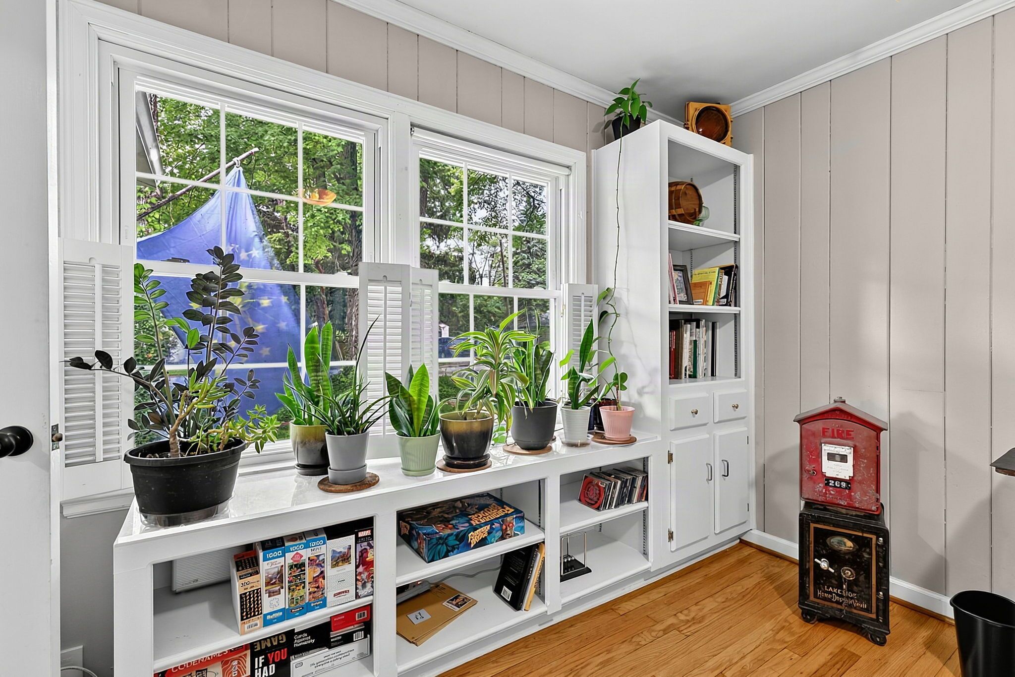 A room with a bay window, a bookshelf, and a fire alarm.