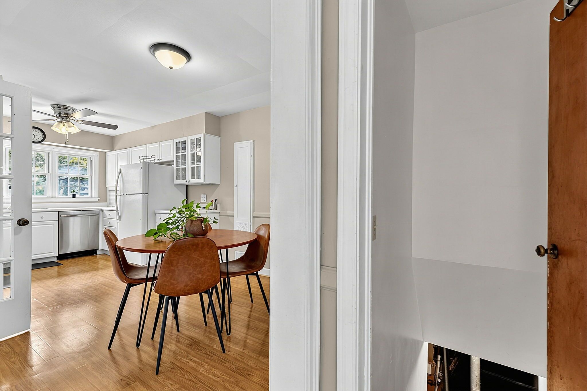 Une cuisine avec des meubles blancs, une table à manger avec des chaises et un ventilateur de plafond.