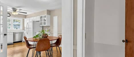 Une cuisine avec des meubles blancs, une table à manger avec des chaises et un ventilateur de plafond.