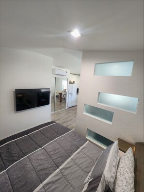 A bedroom with a bed, a flat-screen TV mounted on the wall, and a built-in shelf unit.