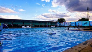 Ein Schwimmbecken mit Rettungsschwimmerstand, Liegestühlen und einem Wandbild von Meereslebewesen.