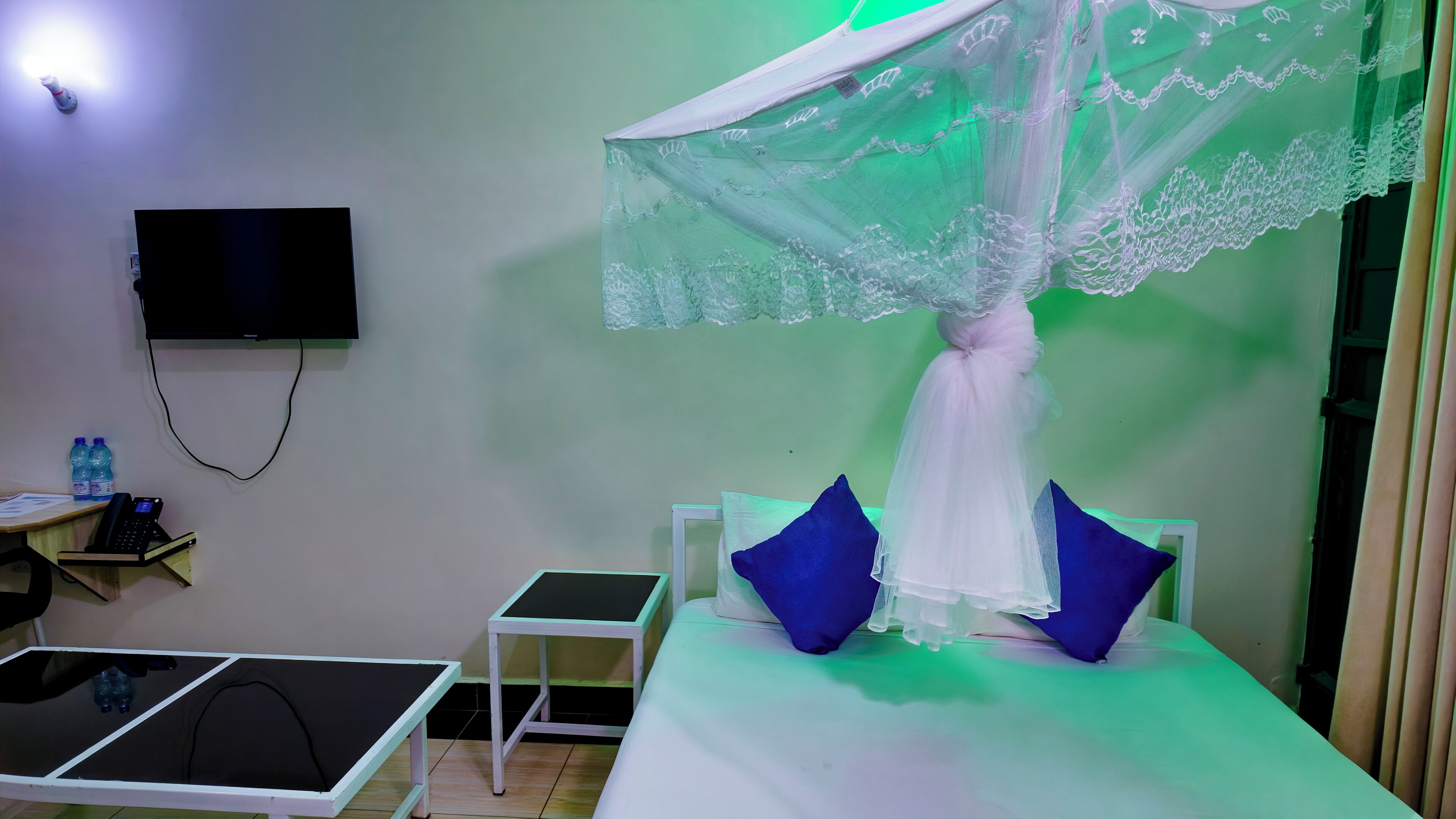 A room with a bed, a small table, a TV mounted on the wall, and a water dispenser.