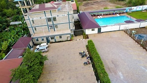 A hotel with a swimming pool, parking area, and a building with a cross-shaped window design.