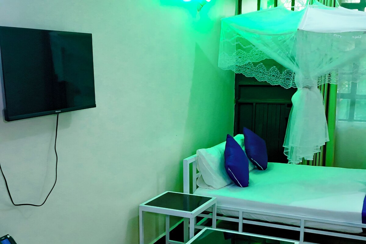 A room with a bed, a TV mounted on the wall, a small table, and a chair.