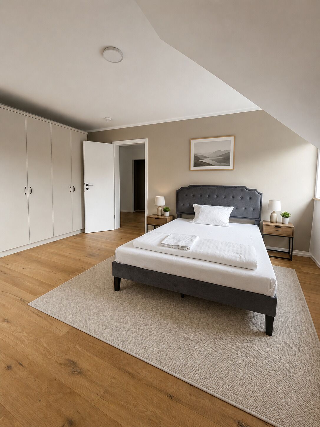 A bedroom with a bed, nightstands, a wardrobe, and a door leading to another room.