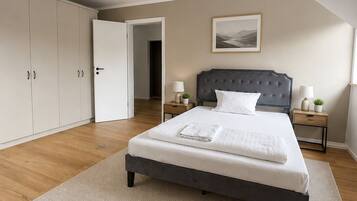 A bedroom with a bed, nightstands, a wardrobe, and a door leading to another room.