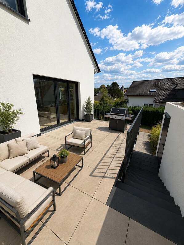 A modern outdoor patio with a sofa set, a coffee table, and a grill.