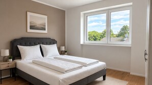 A bedroom with a bed, a nightstand, a lamp, a window, and a picture on the wall. - The Golden Sunset Villa Wiesbaden (Schlangenbad)
