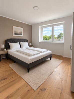 A bedroom with a bed, a nightstand, a lamp, a window, and a picture on the wall. - The Golden Sunset Villa Wiesbaden (Schlangenbad)