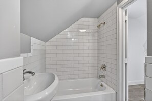 Une salle de bain avec des carreaux de métro blancs, une baignoire blanche et un lavabo blanc.