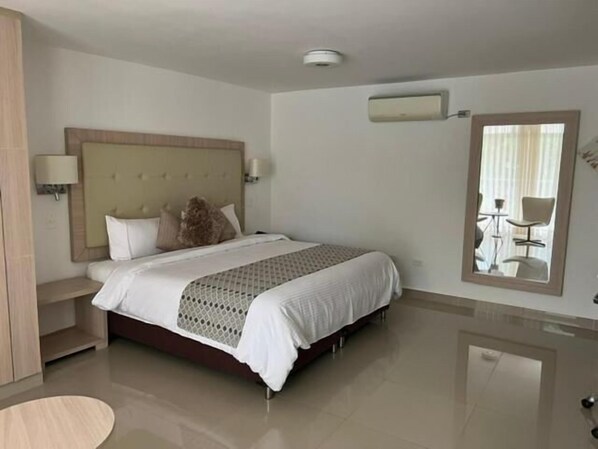 A hotel room with a large bed, bedside tables, a mirror, and a wall-mounted air conditioning unit.