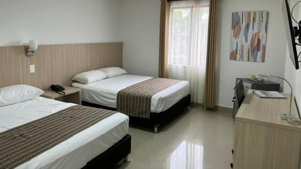 Una habitación de hotel con dos camas, un escritorio, una silla y un ventanal con cortinas.