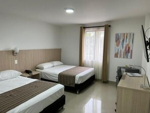 A hotel room with two beds, a desk, a chair, and a window with curtains.