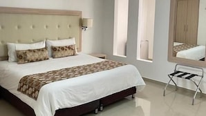 Una habitación de hotel con cama, mesita de noche, lámpara y un espejo grande.