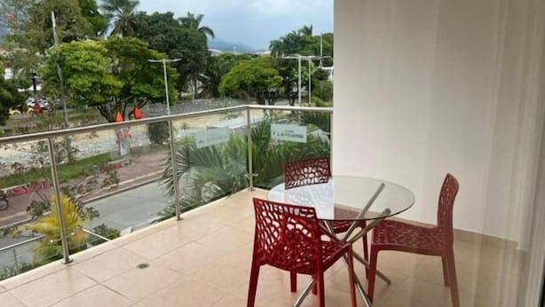 Un balcón con barandilla de vidrio, una mesa y dos sillas.