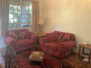 Un salon avec deux canapés rouges, une petite table avec une lampe, un tapis à motifs et une fenêtre avec des rideaux.
