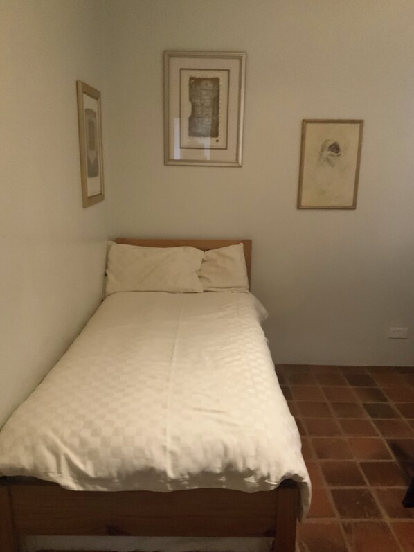A single bed with a wooden headboard in a room with plain walls and a tiled floor.