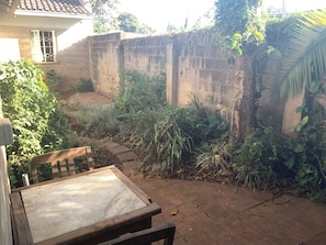 A patio area with a wooden table and chairs, surrounded by a concrete wall and various plants. - Adorable 2-bedroom bungalow in Nairobi perfect for relaxing stays (Nairobi)