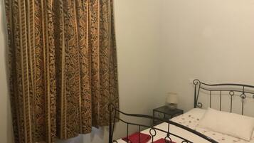 A single bed with a metal frame, a bedside table with a lamp, and a patterned curtain.