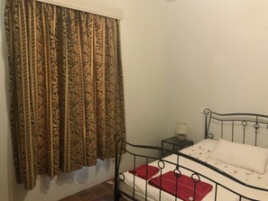 A single bed with a metal frame, a bedside table with a lamp, and a patterned curtain. - Adorable 2-bedroom bungalow in Nairobi perfect for relaxing stays (Nairobi)