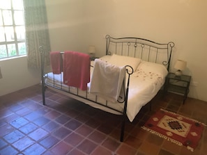 A single bed with a metal frame, a bedside table with a lamp, and a patterned rug on a tiled floor.