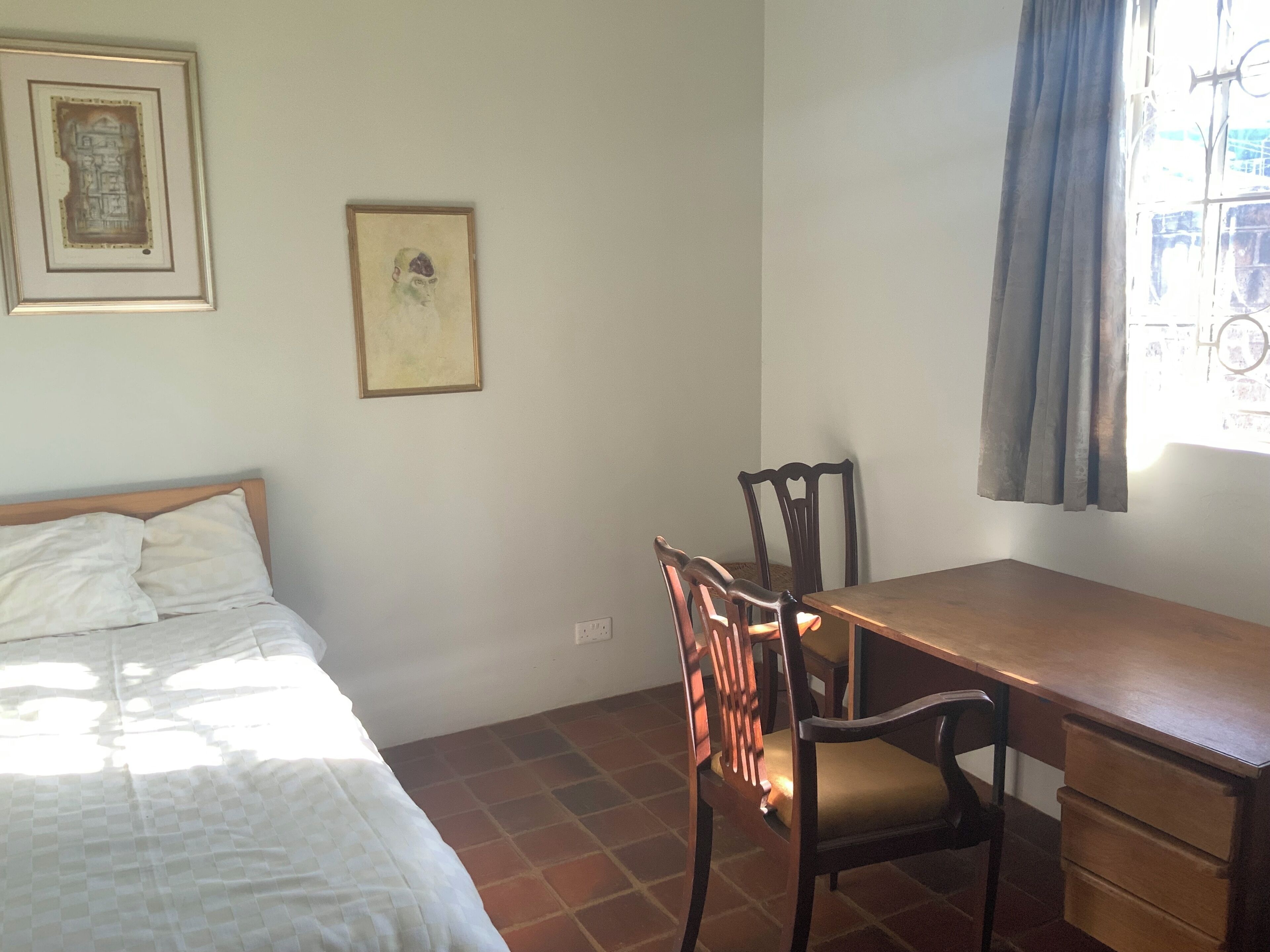 A room with a bed, a desk, and chairs. There are two framed pictures on the wall.