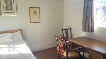 A room with a bed, a desk, and chairs. There are two framed pictures on the wall.