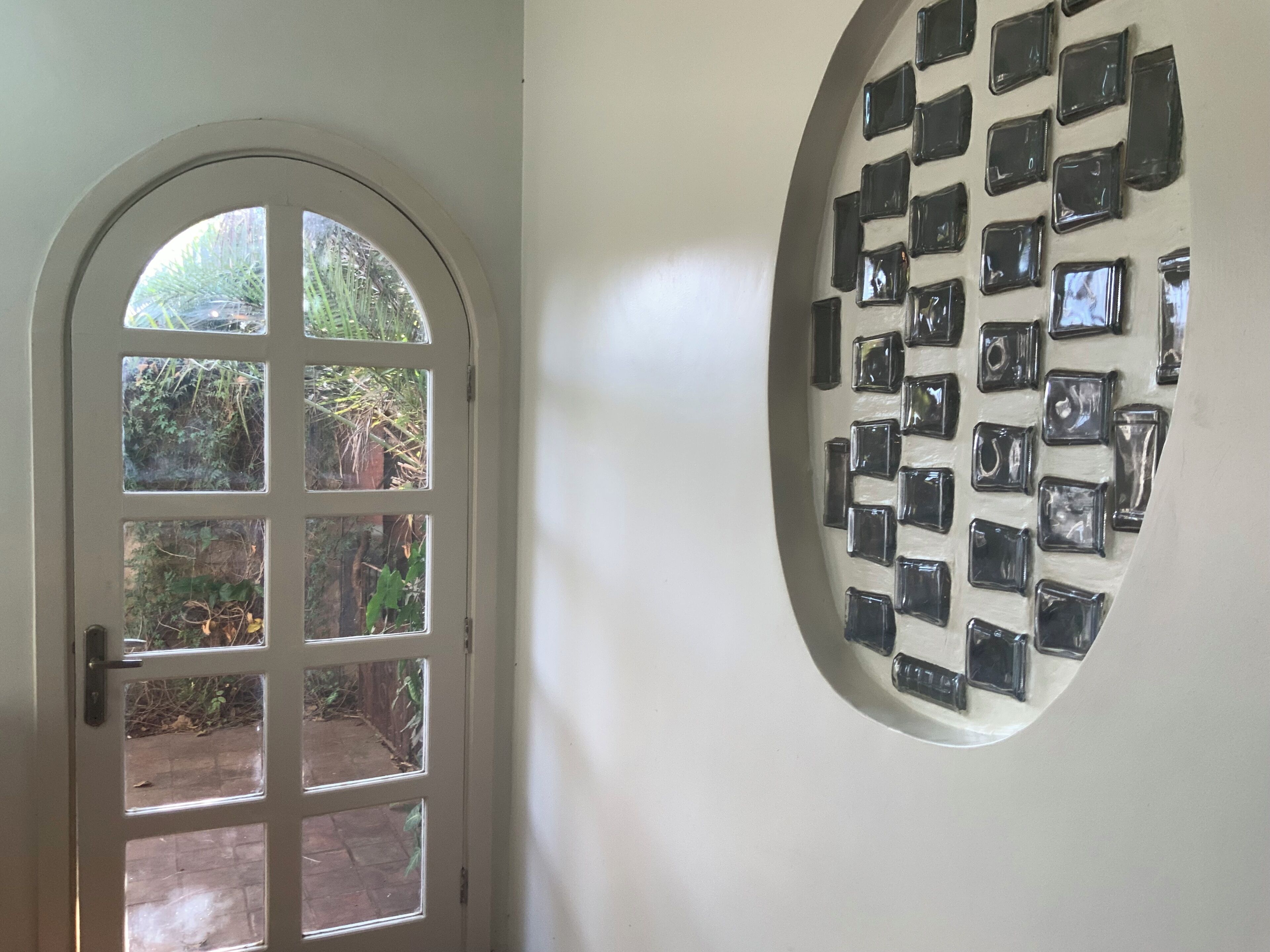 A door with a view of a garden and a wall with multiple square mirrors.