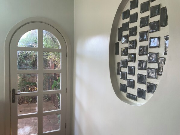 A door with a view of a garden and a wall with multiple square mirrors.