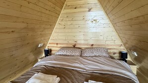Ein Zimmer mit dreieckiger Decke, einem Bett, Kissen und zwei Nachttischlampen.
