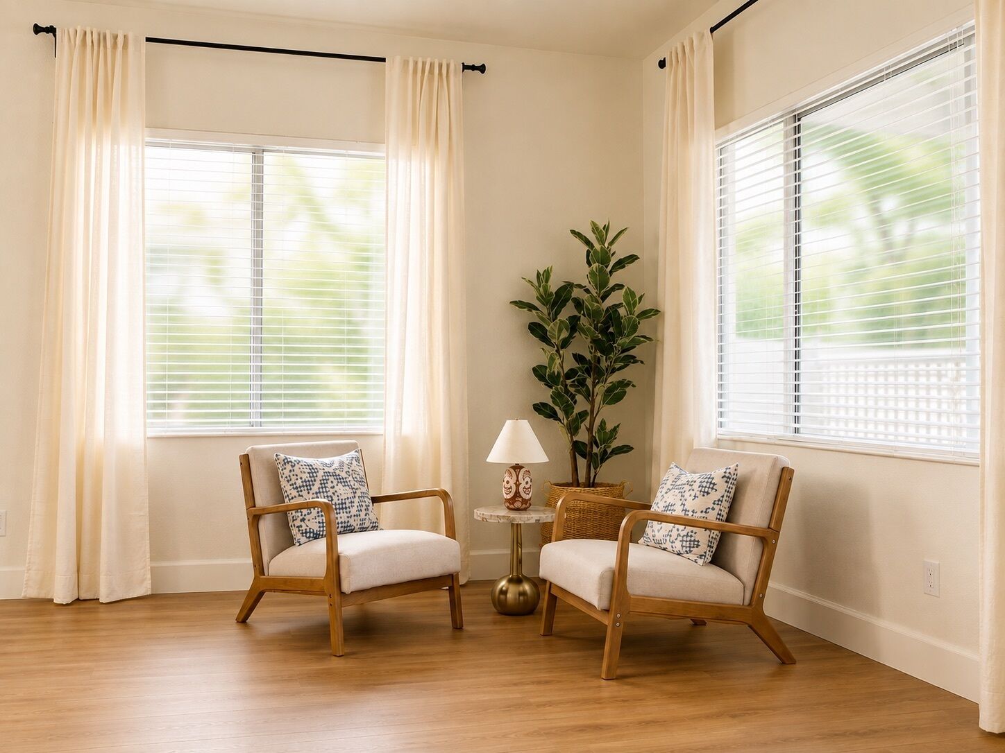 A room with two wooden chairs, a small table with a lamp, and a potted plant.