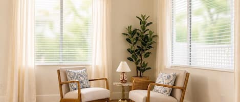A room with two wooden chairs, a small table with a lamp, and a potted plant.