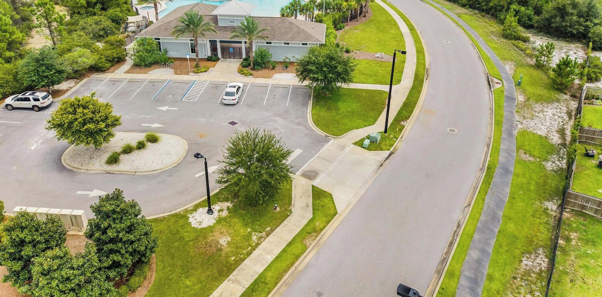 An aerial view of a parking lot with a building in the background, a curved road, and surrounding greenery.