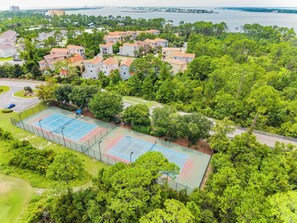Zona residencial con cancha de tenis, rodeada de vegetación exuberante y un cuerpo de agua al fondo.