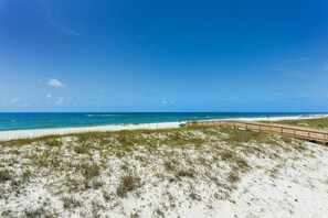 Ein Strand mit einem hölzernen Steg, der zum Meer führt, Sanddünen und klarem, blauem Wasser.