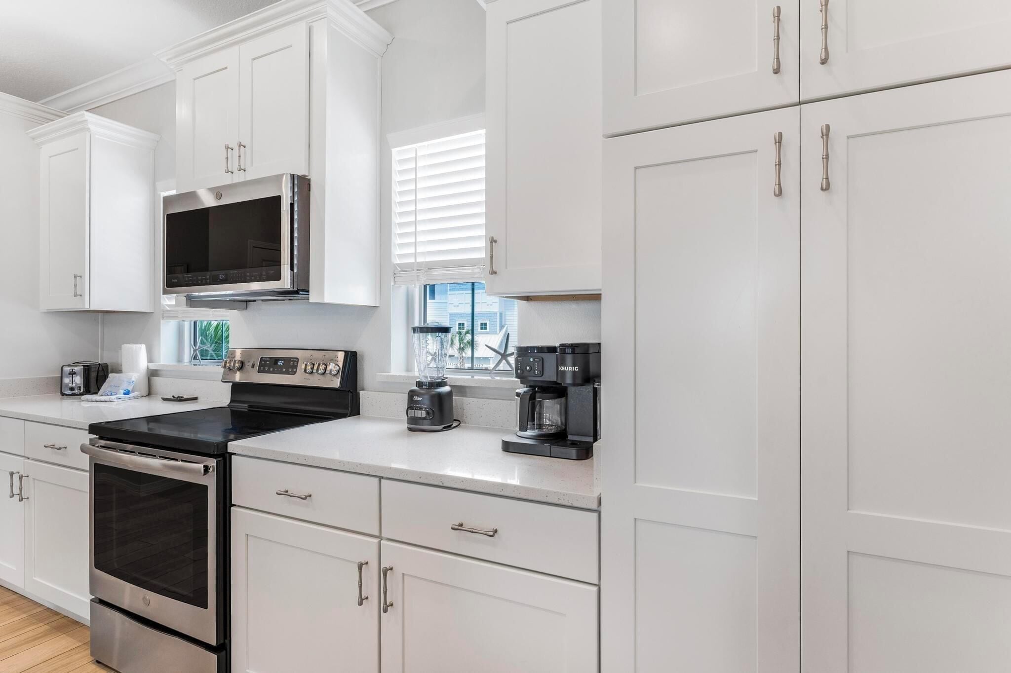 A modern kitchen with white cabinetry, a stainless steel oven, a microwave, a coffee maker, and a blender.