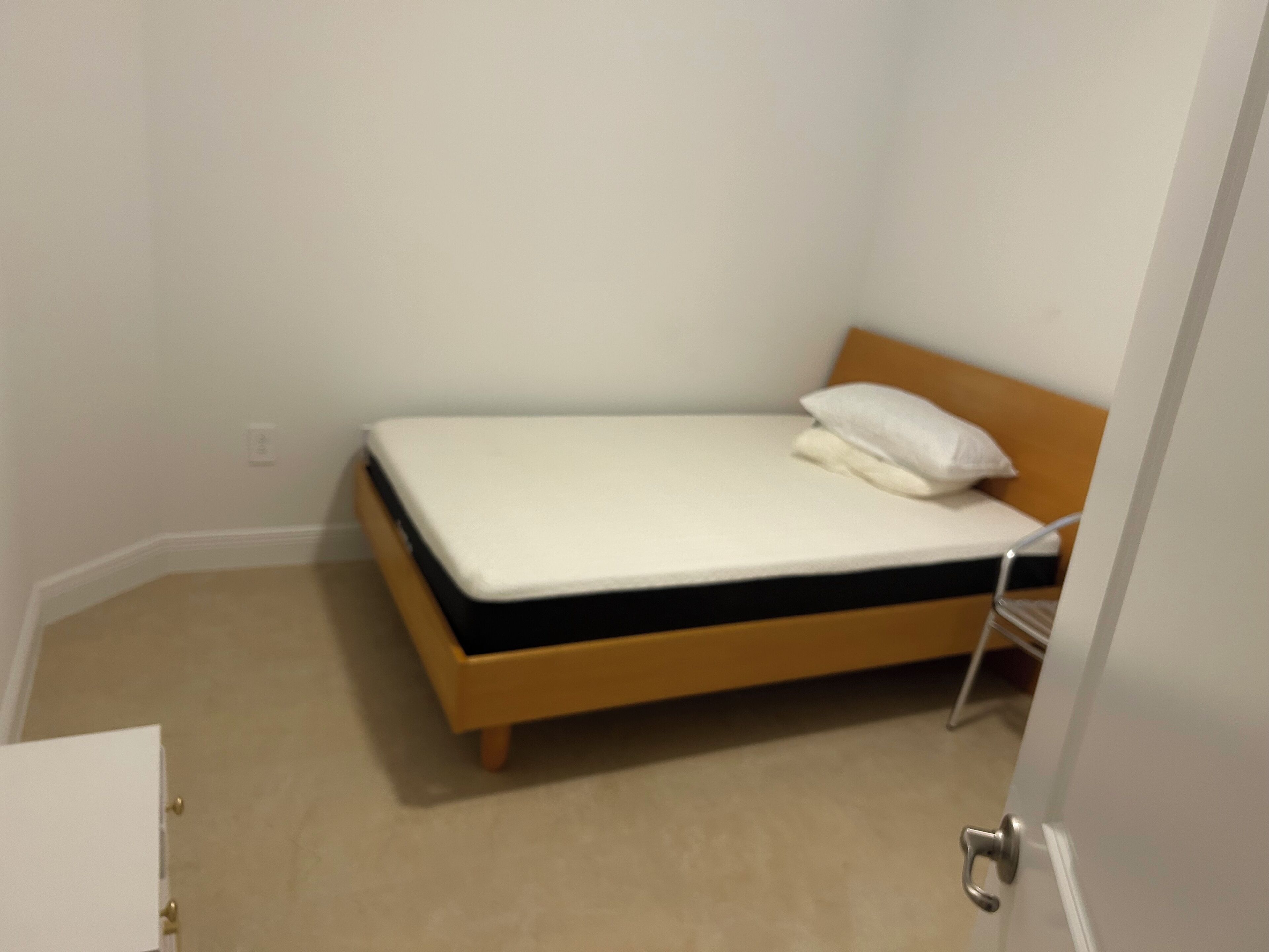 Una habitación pequeña con cama individual, cabecera de madera y colchón blanco.