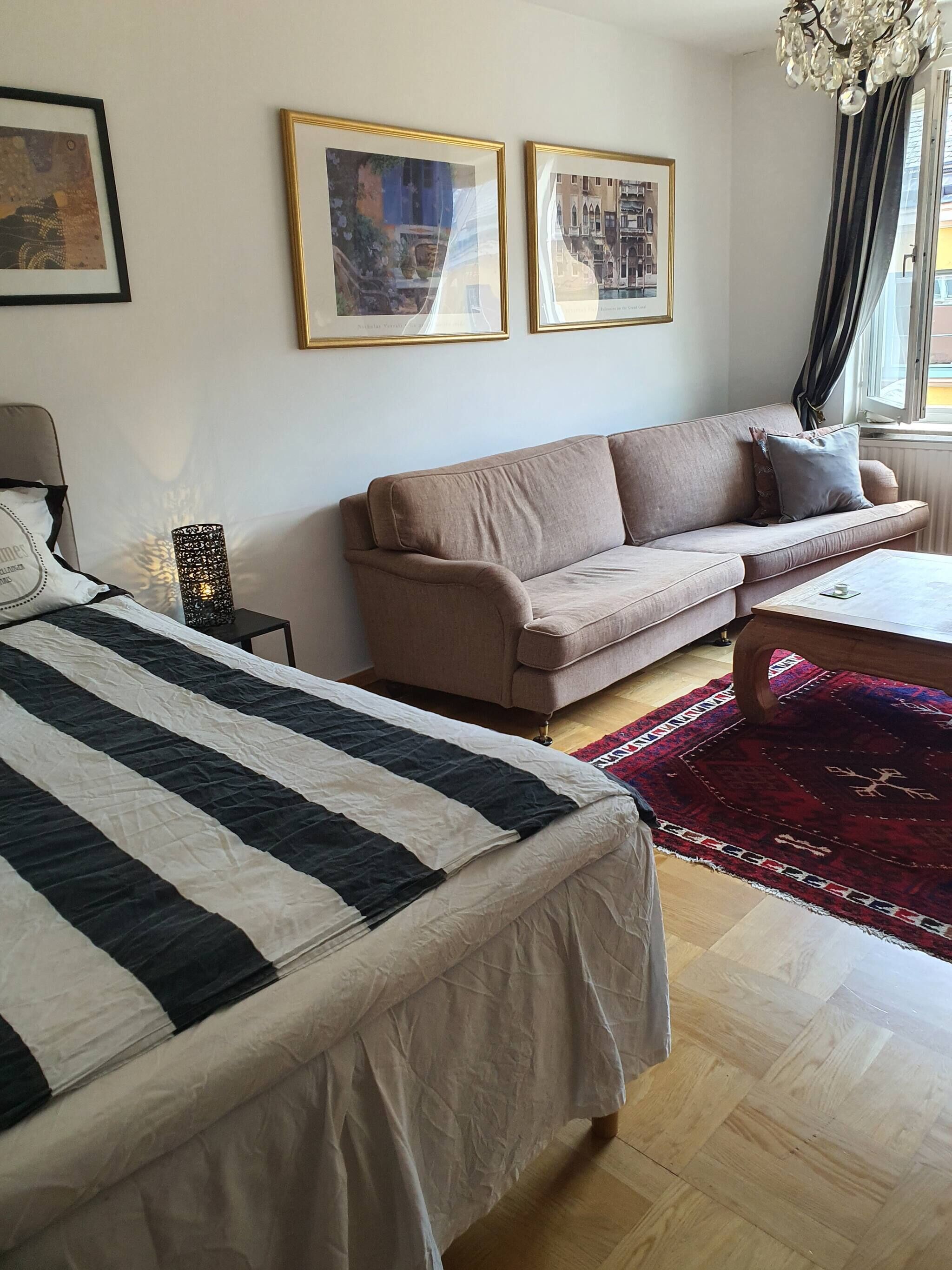 Un dormitorio con cama, sofá, una mesita de centro y dos cuadros en la pared.