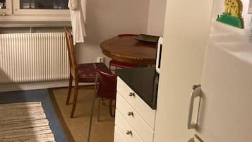 Una cocina compacta con refrigerador, una mesa de comedor con sillas, una lámpara colgante y un radiador.