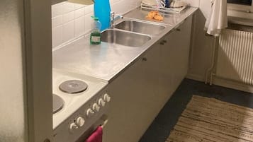 Una cocina funcional con estufa, pileta y ventana con cortinas.