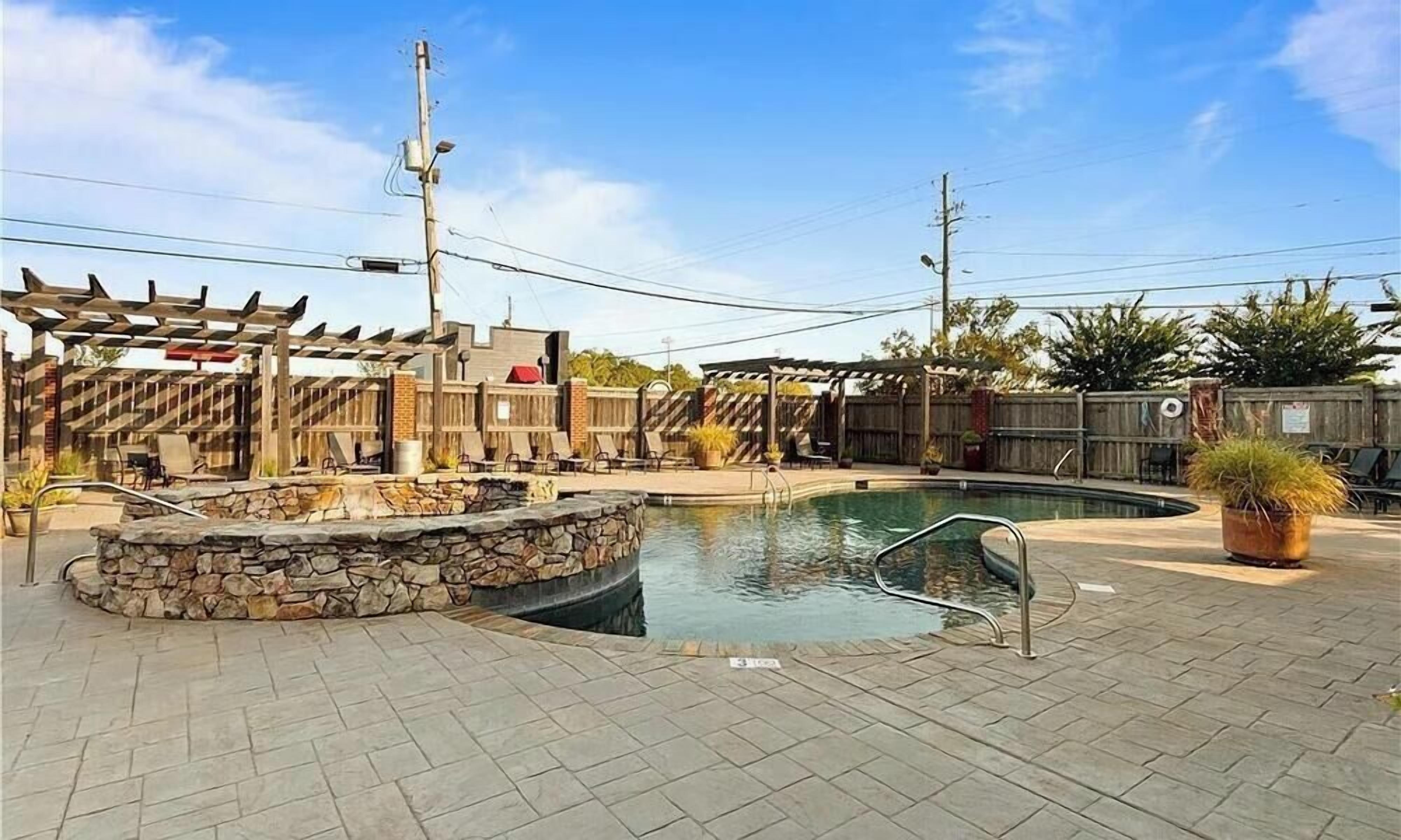Ein Poolbereich mit einem Steinsbrunnen, einer Holzpergola und einer umzäunten Terrasse.