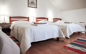 Quarto de hotel com duas camas, cabeceira de madeira, mesa de cabeceira, abajur e quadro na parede.