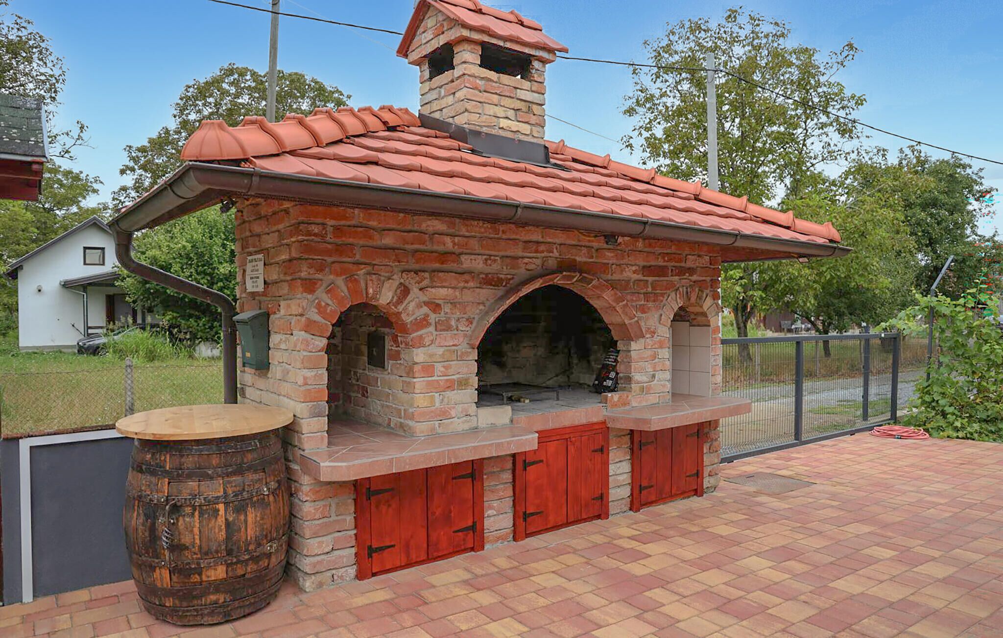 A brick-built outdoor oven with a chimney, red doors, and a barrel.
