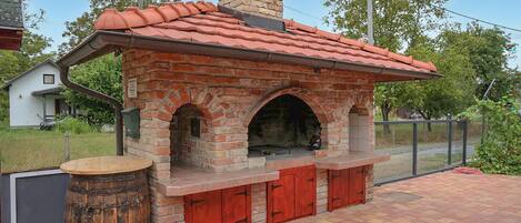 A brick-built outdoor oven with a chimney, red doors, and a barrel.